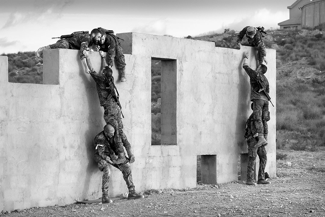 Service members helping one another over a wall.